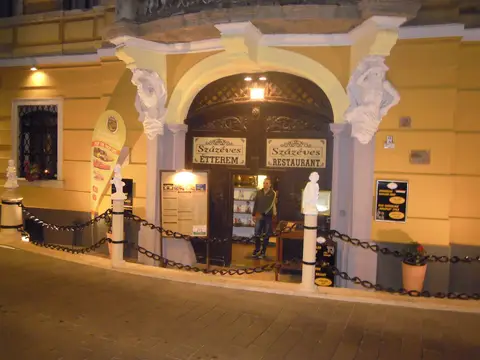 Arched doorway flanked by stone figures, boards lettered Százéves Étterem and Százéves Restaurant