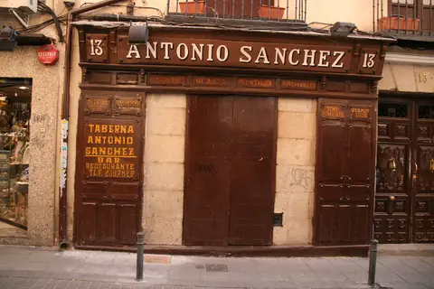 Carved dark-wood shopfront lettered ANTONIO SANCHEZ 13, shutters closed, wine names painted on the panels