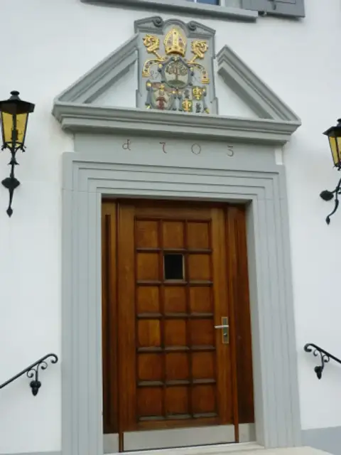 Oak door below a painted coat of arms and the date 1703, a lantern on either side