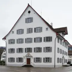 White gabled tavern with grey shutters and a panelled oak door under a carved 1703 pediment