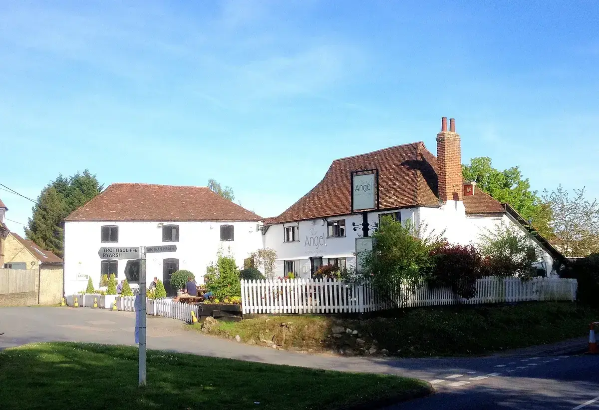 White rendered pub with a steep tiled roof and brick chimney behind a white picket fence