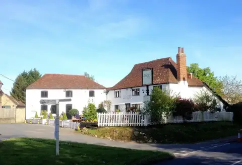 White rendered pub with a steep tiled roof and brick chimney behind a white picket fence