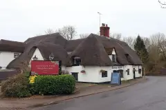 White-painted thatched pub with sweeping roofs and a brick chimney, beside a village lane