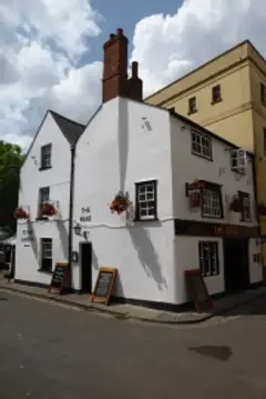 Small whitewashed corner pub with a tall brick chimney, black-framed windows and chalkboards