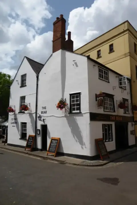 Small whitewashed corner pub with a tall brick chimney, black-framed windows and chalkboards