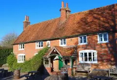 Red-brick pub with a tiled roof, tall chimneys, timber porch and a bell set in the wall