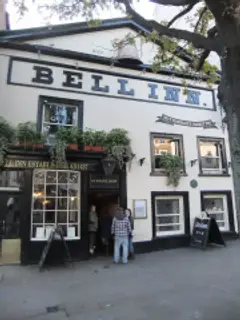Cream-painted inn front with large black lettering, a gilded bell on the parapet and window plants
