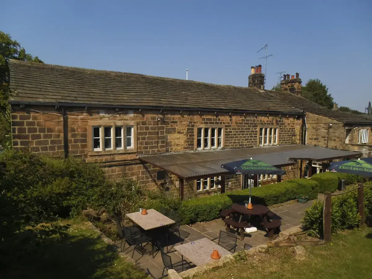 Long gritstone rear range with mullioned windows above a paved terrace of tables and parasols