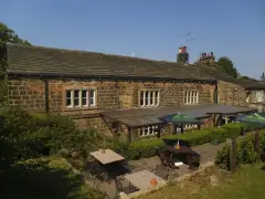 Long gritstone rear range with mullioned windows above a paved terrace of tables and parasols