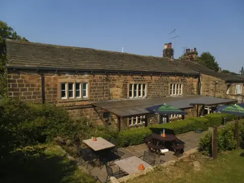 Long gritstone rear range with mullioned windows above a paved terrace of tables and parasols