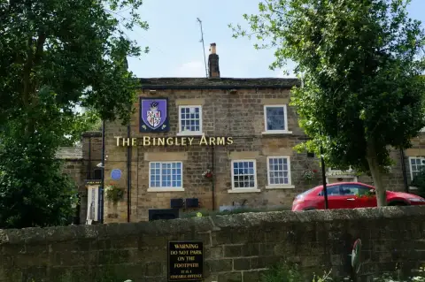 Two-storey gritstone frontage with sash windows, gold lettering and a painted coat-of-arms sign