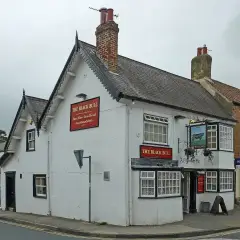Whitewashed corner inn with bargeboarded gables, red name boards and a bull sign in a wrought-iron bracket