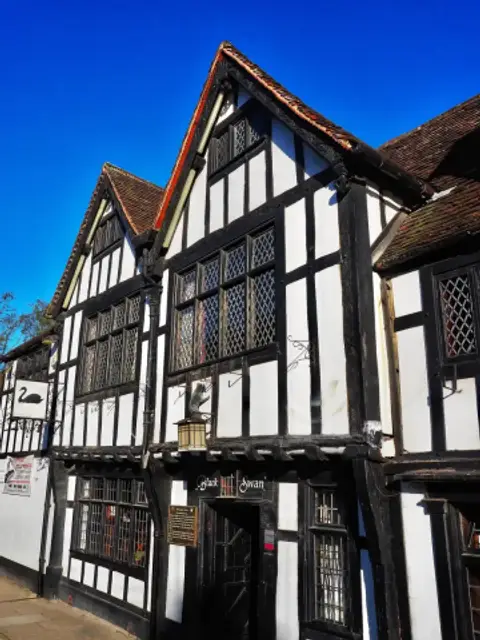 The Black Swan’s jettied timber front in low sun, its swan sign at the left and a carved beast by the lantern