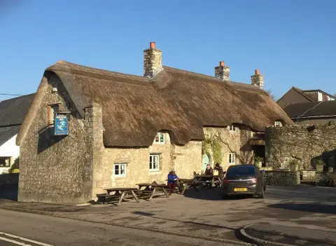 The same thatched stone inn in low winter sun, with benches and a car on the forecourt