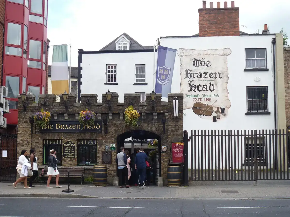 Stone-fronted pub with a battlemented parapet and arched carriageway, beside a painted gable sign