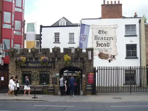 Stone-fronted pub with a battlemented parapet and arched carriageway, beside a painted gable sign
