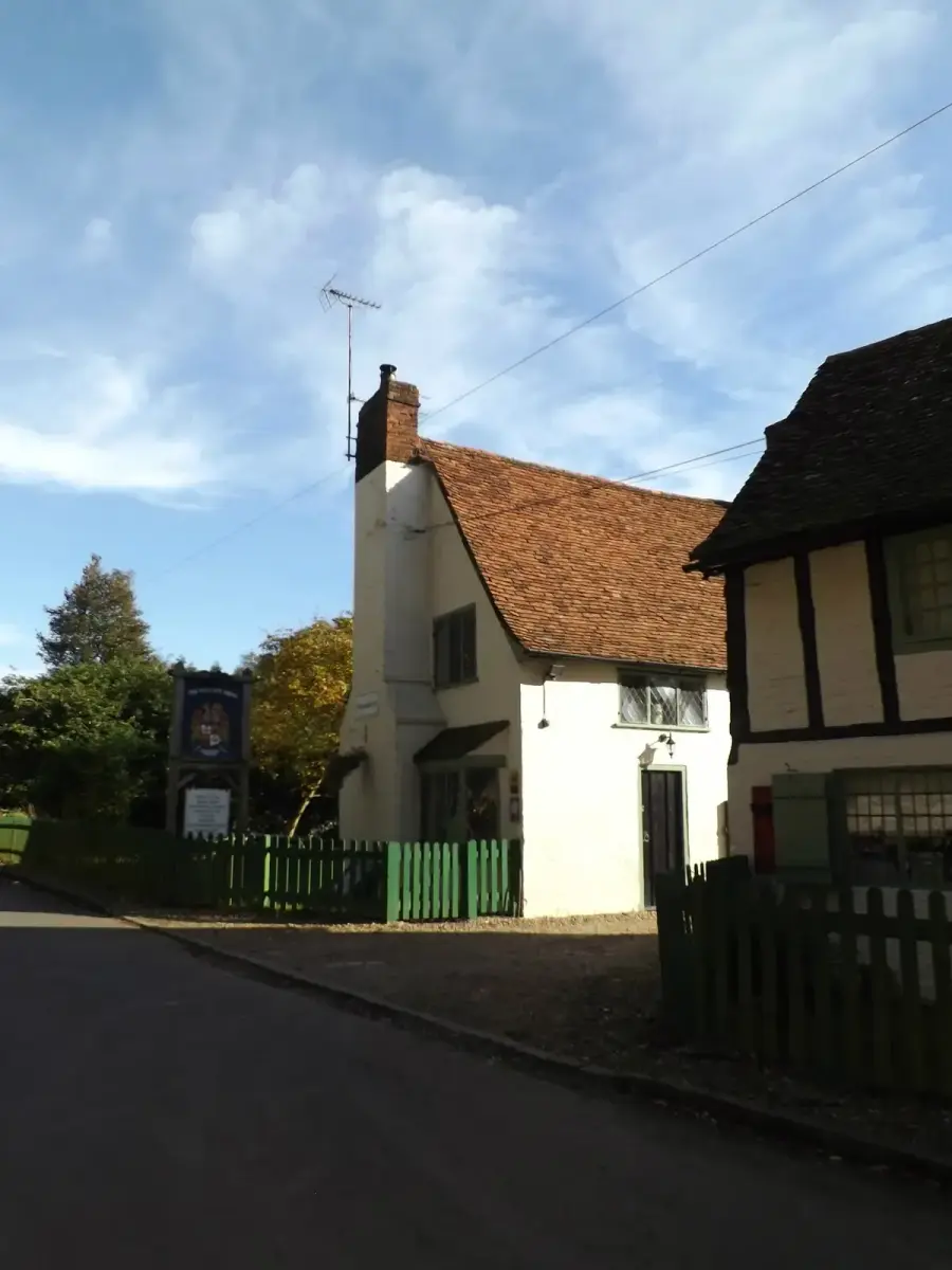 Cream-washed gable end with a tall chimney and leaded windows, behind a green picket fence