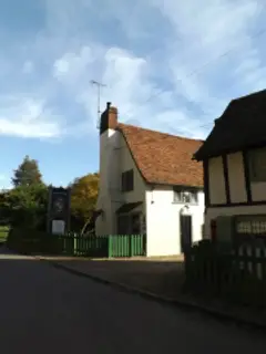 Cream-washed gable end with a tall chimney and leaded windows, behind a green picket fence
