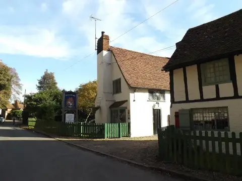 Cream and timber-framed pub with a tiled roof beside a lane, its painted sign on a post