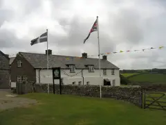 Long whitewashed inn with a slate roof behind a low stone wall, Cornish and Union flags flying