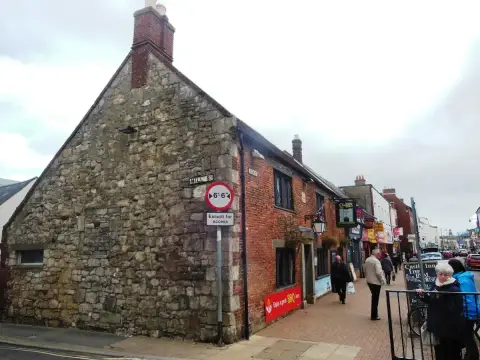 Rubble-stone gable end with a brick chimney on a street corner, the inn's sign further along