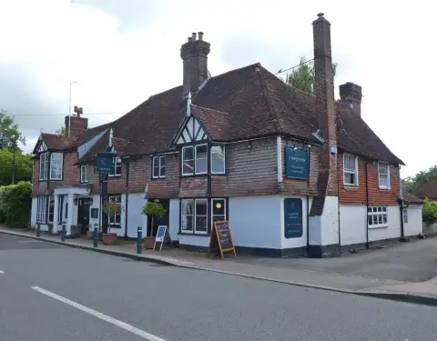 Tile-hung and weatherboarded inn on a corner with a blue name sign and a pavement blackboard