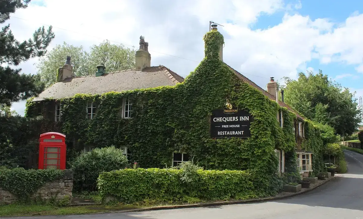 Stone inn almost covered in creeper, with stone-slate roof, tall chimneys and a red phone box