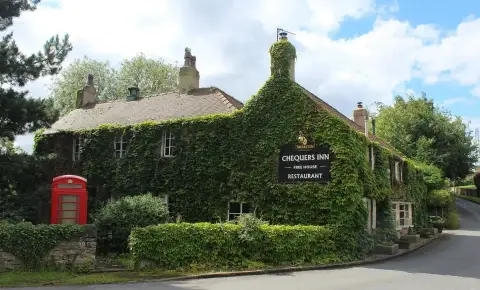 Stone inn almost covered in creeper, with stone-slate roof, tall chimneys and a red phone box