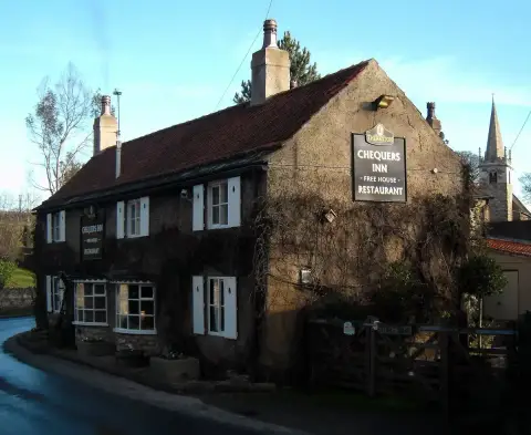 The same inn in winter with bare creeper stems, pantiled roof and the church spire behind