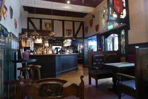 Bar room with exposed timber framing, painted college shields on the walls and leather settles