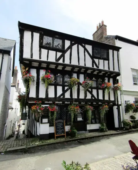 Three-storey timber-framed inn with two jettied floors, leaded windows and hanging baskets