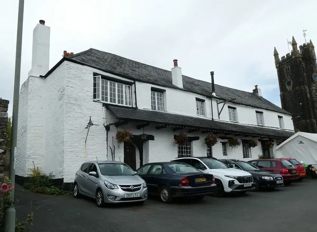 Long whitewashed inn with a slate roof and deep eaves, the church tower rising behind it