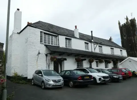 Long whitewashed inn with a slate roof and deep eaves, the church tower rising behind it