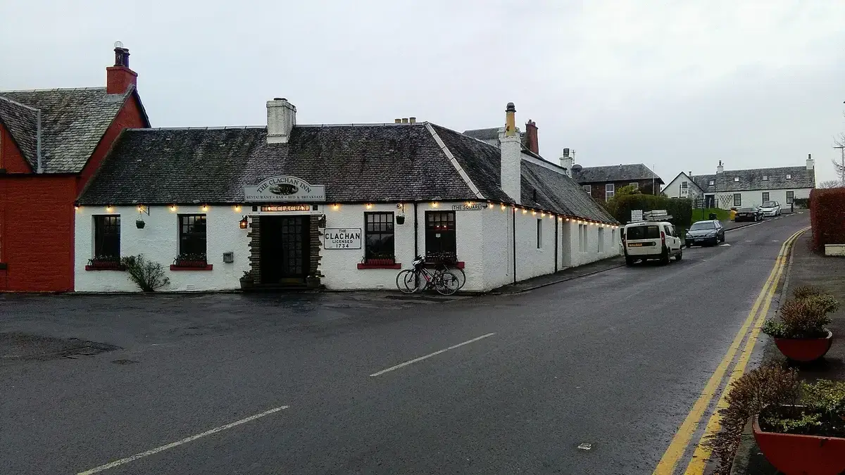 Long low whitewashed inn with a slate roof and strings of lights, on the square in a village