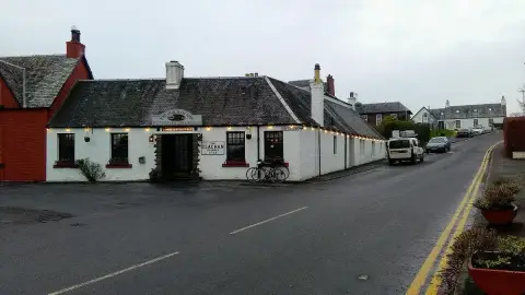 Long low whitewashed inn with a slate roof and strings of lights, on the square in a village