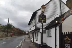 Weatherboarded pub on a wet street corner under grey cloud, hanging sign on a cast-iron lamp post
