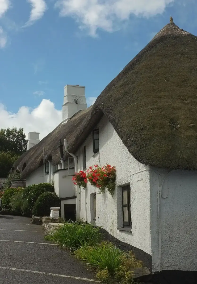 Long thatched and whitewashed inn curving along a lane, with white chimneys and window boxes