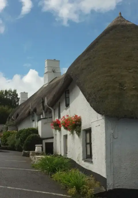 Long thatched and whitewashed inn curving along a lane, with white chimneys and window boxes