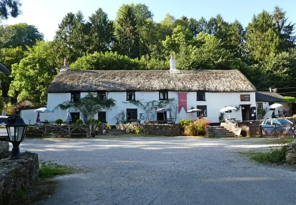 Long thatched white inn in a wooded valley, with parasols and tables on the gravel forecourt