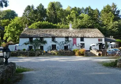 Long thatched white inn in a wooded valley, with parasols and tables on the gravel forecourt