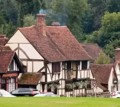 Timber-framed inn with a deep tiled roof and jettied upper floor, seen across the village green
