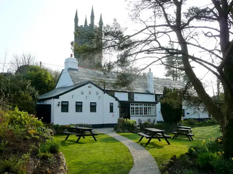 The whitewashed Crown Inn at Lanlivery with picnic benches and the church tower behind