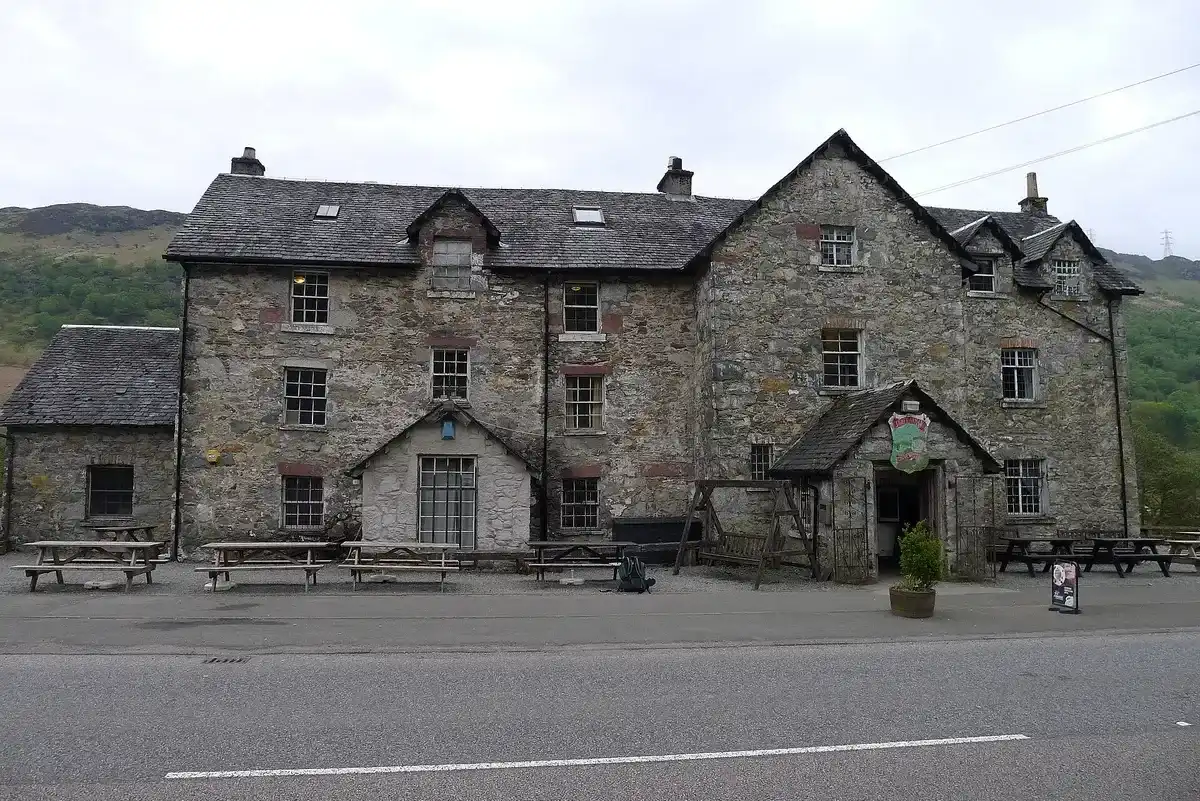 Three-storey rubble-stone inn with slate roof, dormers and picnic benches along the roadside