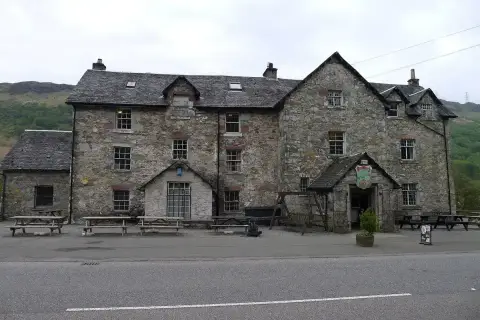 Three-storey rubble-stone inn with slate roof, dormers and picnic benches along the roadside