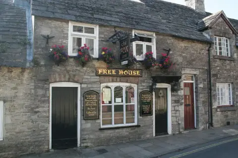 Purbeck stone frontage with a stone-slate roof, gold-lettered boards and hanging baskets