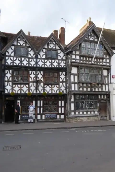 Two timber-framed houses with decorative curved bracing and gables, on a town street