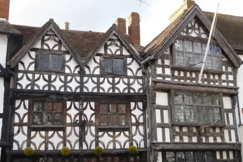 Close view of ornate timber framing with carved bargeboards and leaded windows on two gables