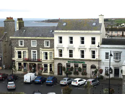 The inn's stone front beside the Isle of Man Bank on Castletown square, the sea behind the roofs