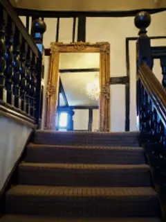 Carpeted staircase with a heavy turned balustrade rising to a timber-framed landing and mirror