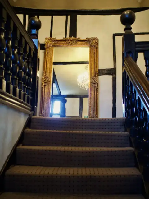 Carpeted staircase with a heavy turned balustrade rising to a timber-framed landing and mirror